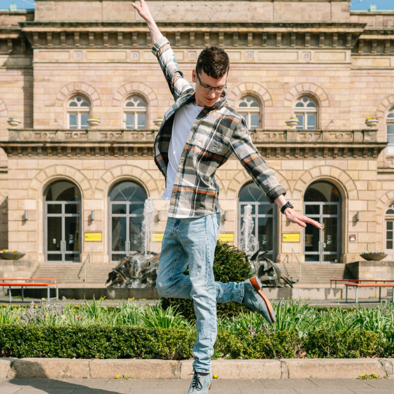 Junger Mann in gestreiftem Hemd tanzt fröhlich vor einem historischen Gebäude. Junger Mann in gestreiftem Hemd tanzt fröhlich vor einem historischen Gebäude.